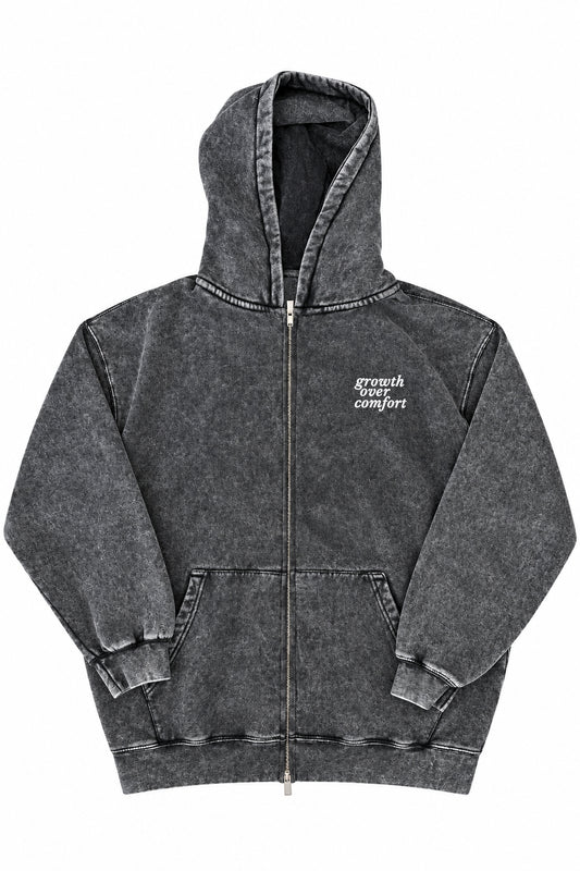 A dark gray acid-wash zip-up hoodie with a small white embroidered graphic on the left chest, laid flat on a light wood floor.
